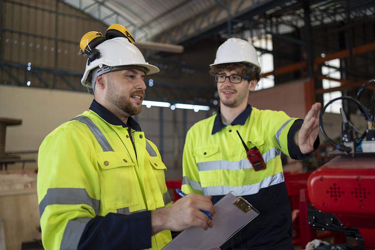 Engineer or technician worker check the robotic arm function of machine and co-worker support in the back in factory workplace